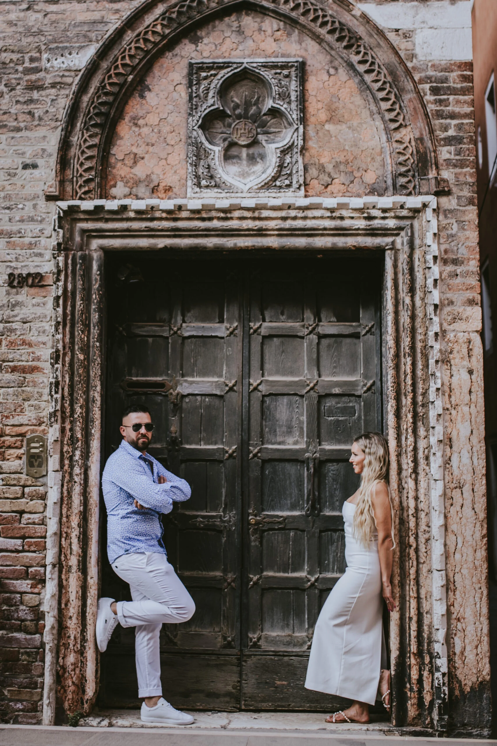 Couple standing on either side of an old Venetian doorway