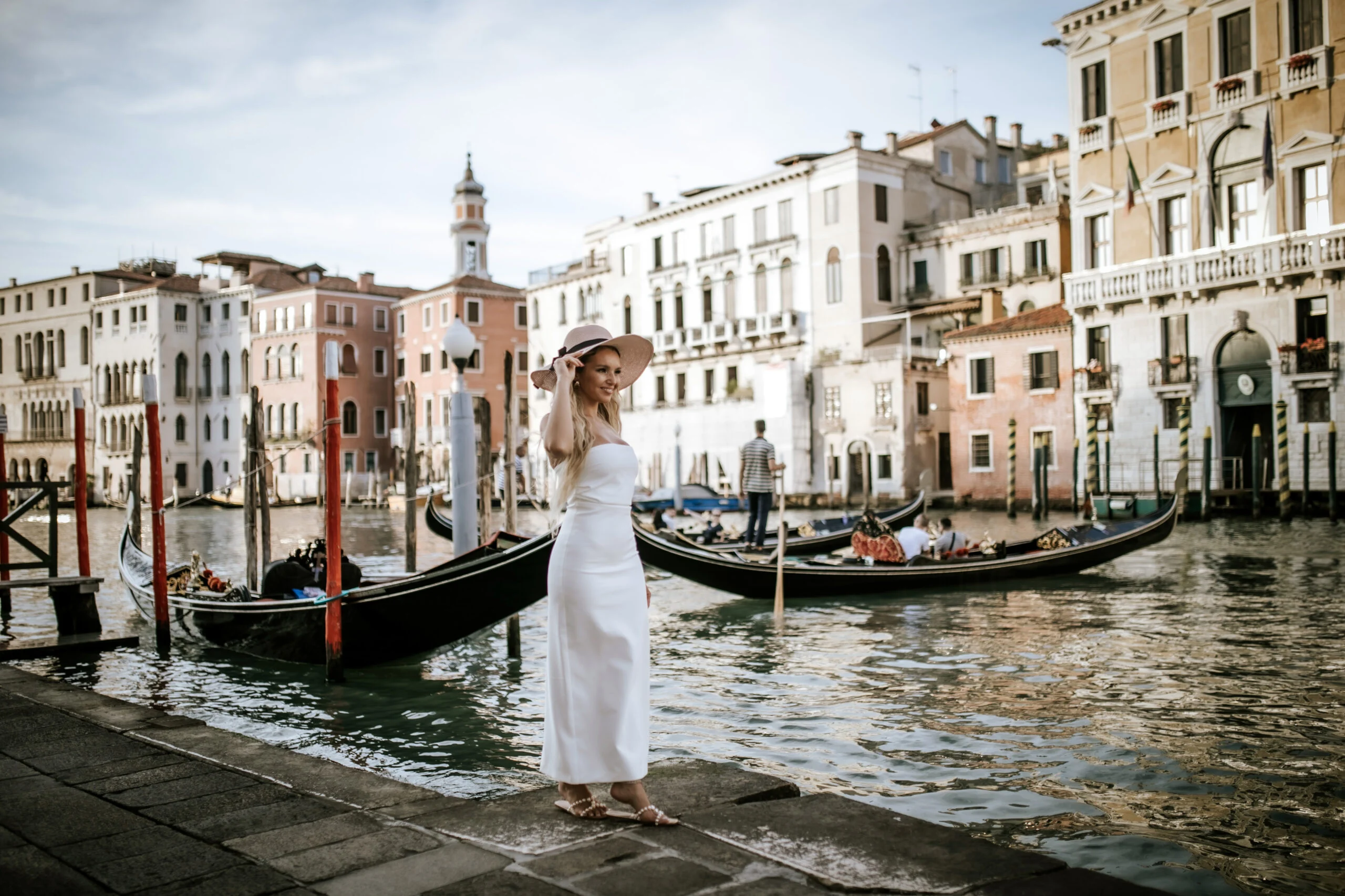 Woman standing at the water's edge beside a moored gondola