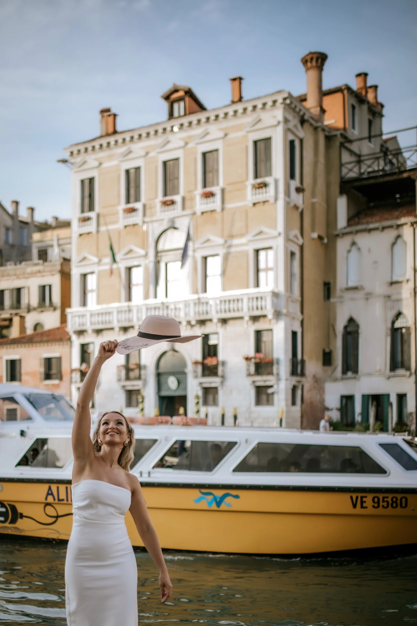 Woman throwing her hat in the air beside the canal