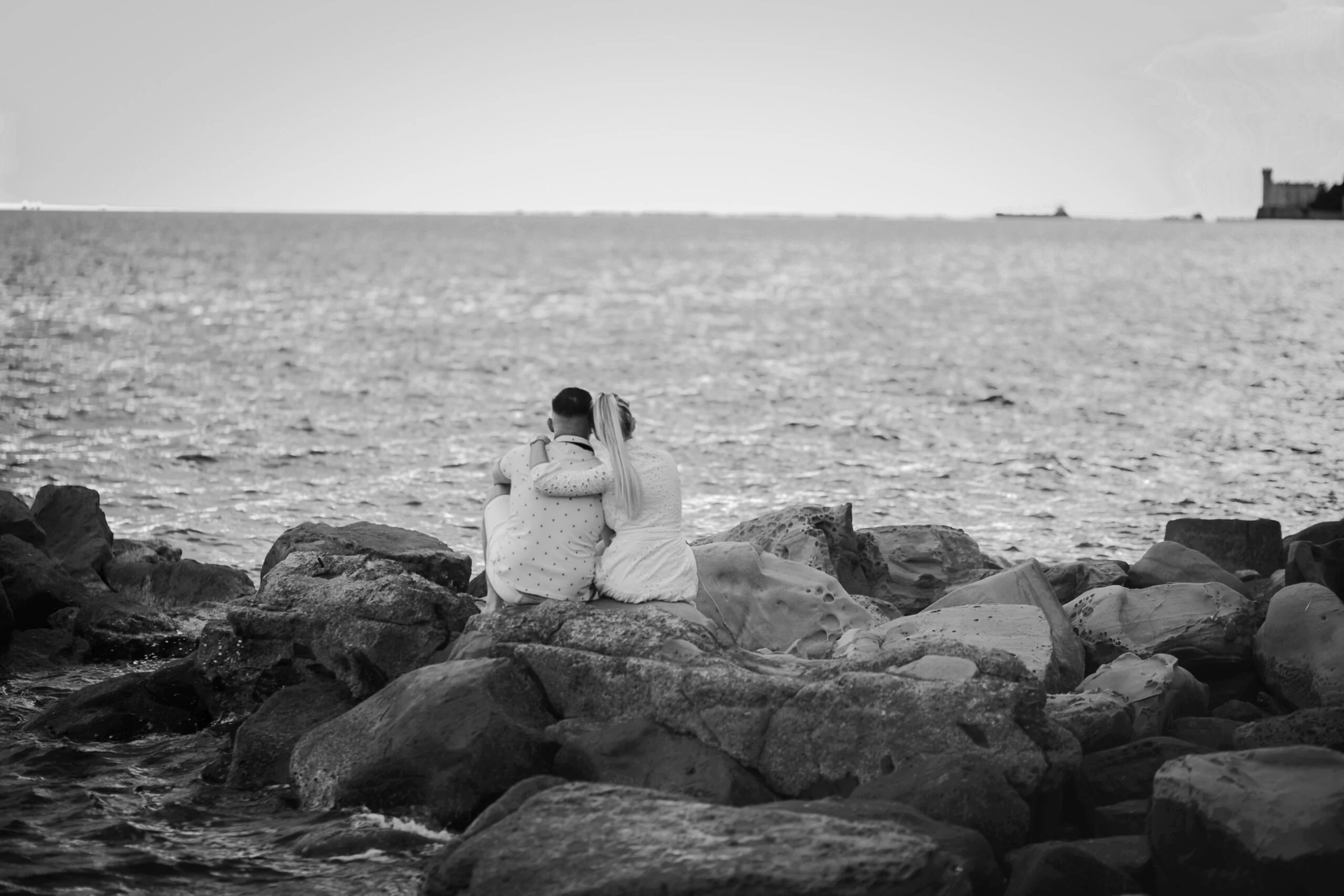 Black and white photograph of the couple sitting on the rocks looking out to sea