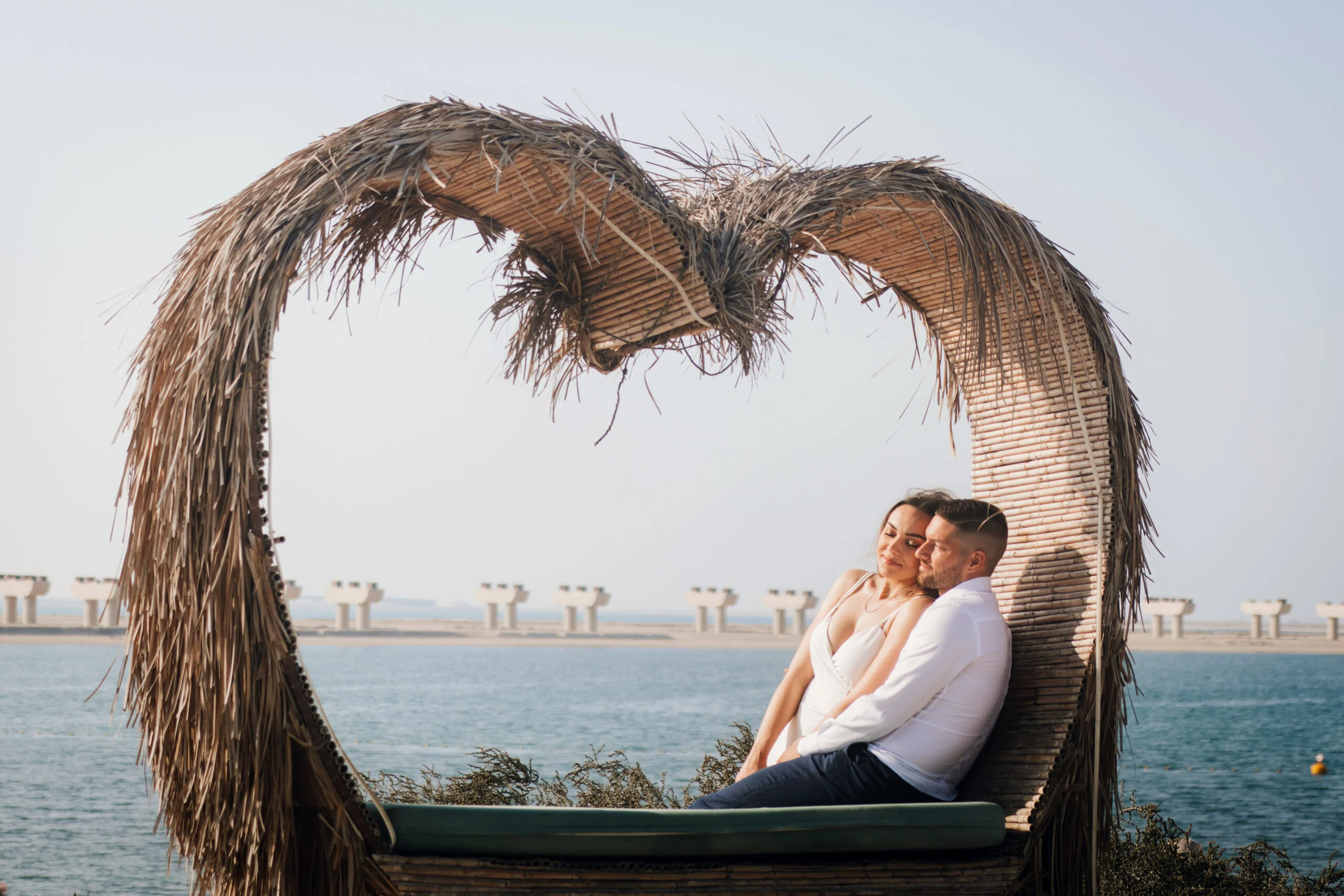 Couple sitting together in a heart-shaped shelter on the beach