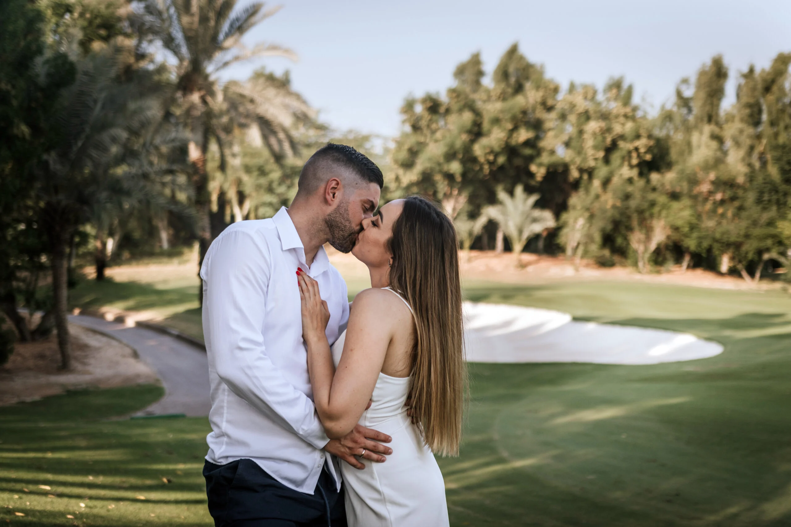 Couple kissing on the golf course, palms behind them