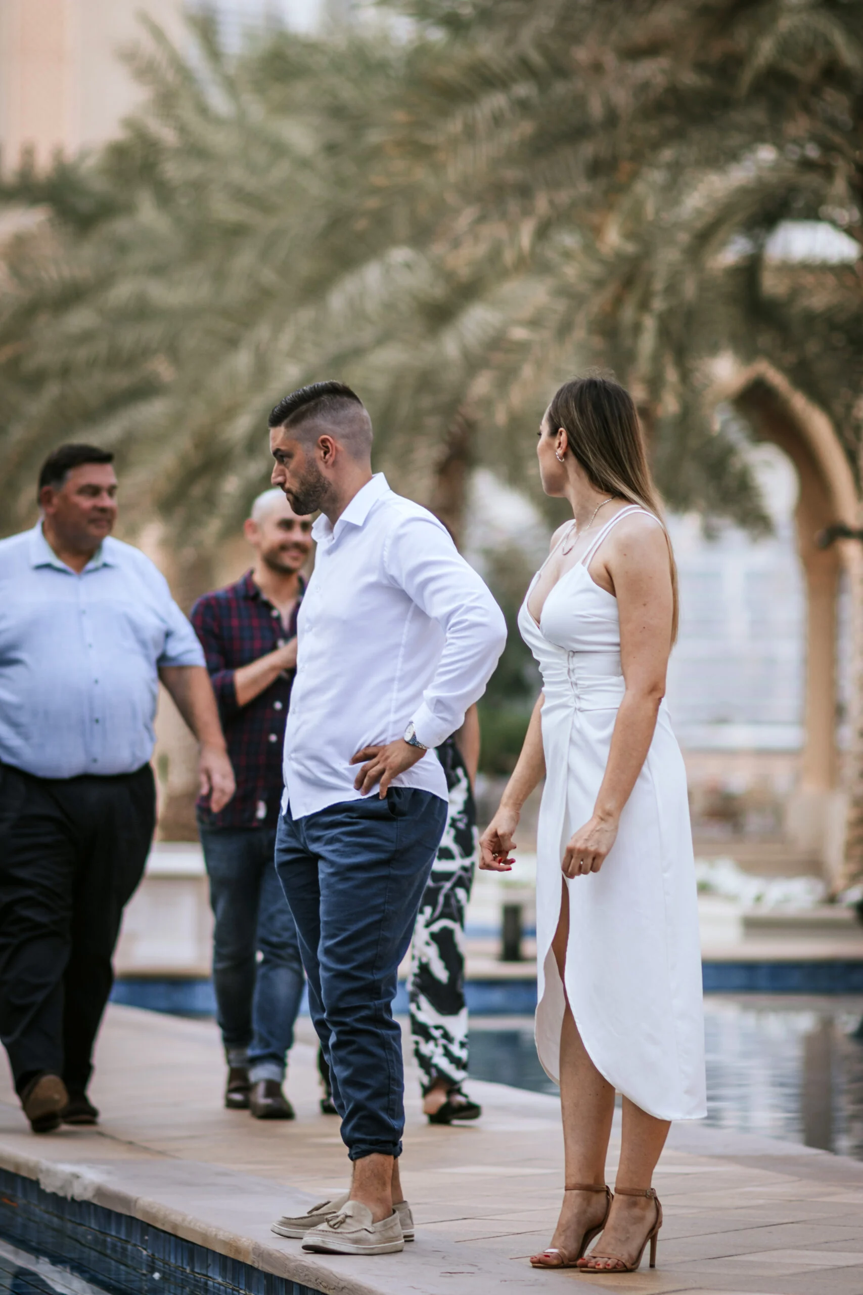 Couple walking beside a pool, passers-by behind them