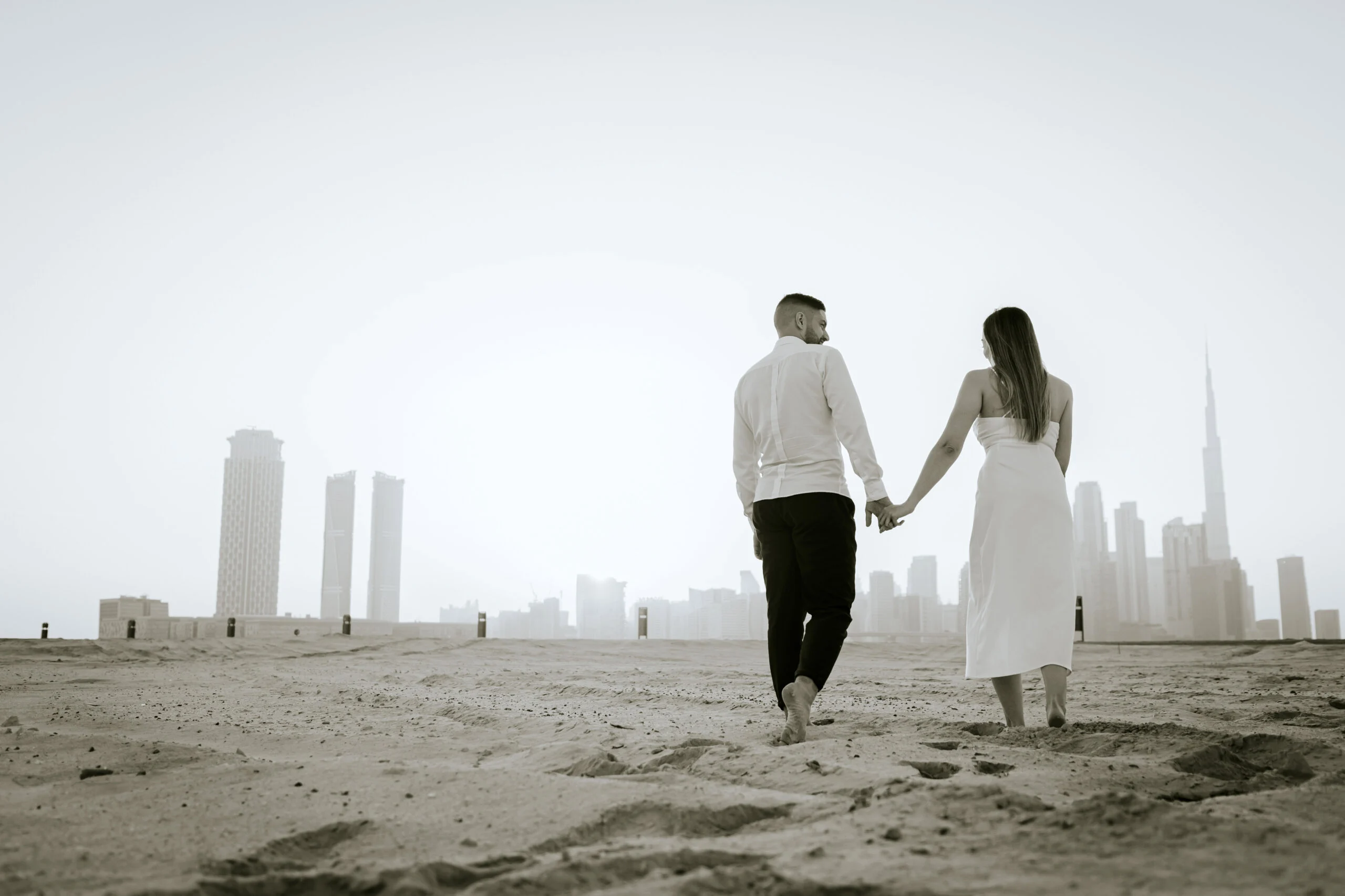 Couple walking hand in hand on the sand, the city in the haze