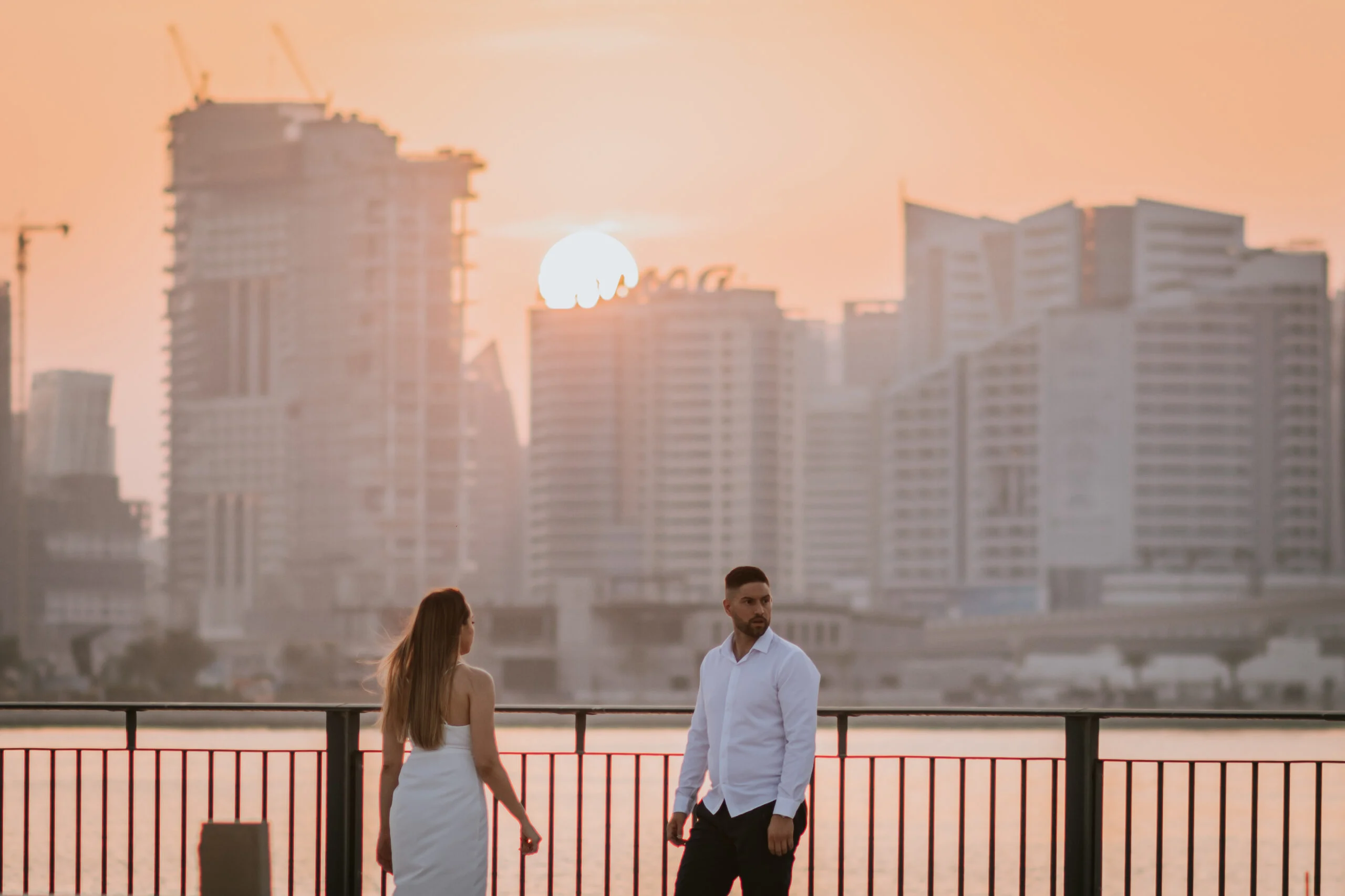 Couple by the waterfront as the sun sets behind the towers