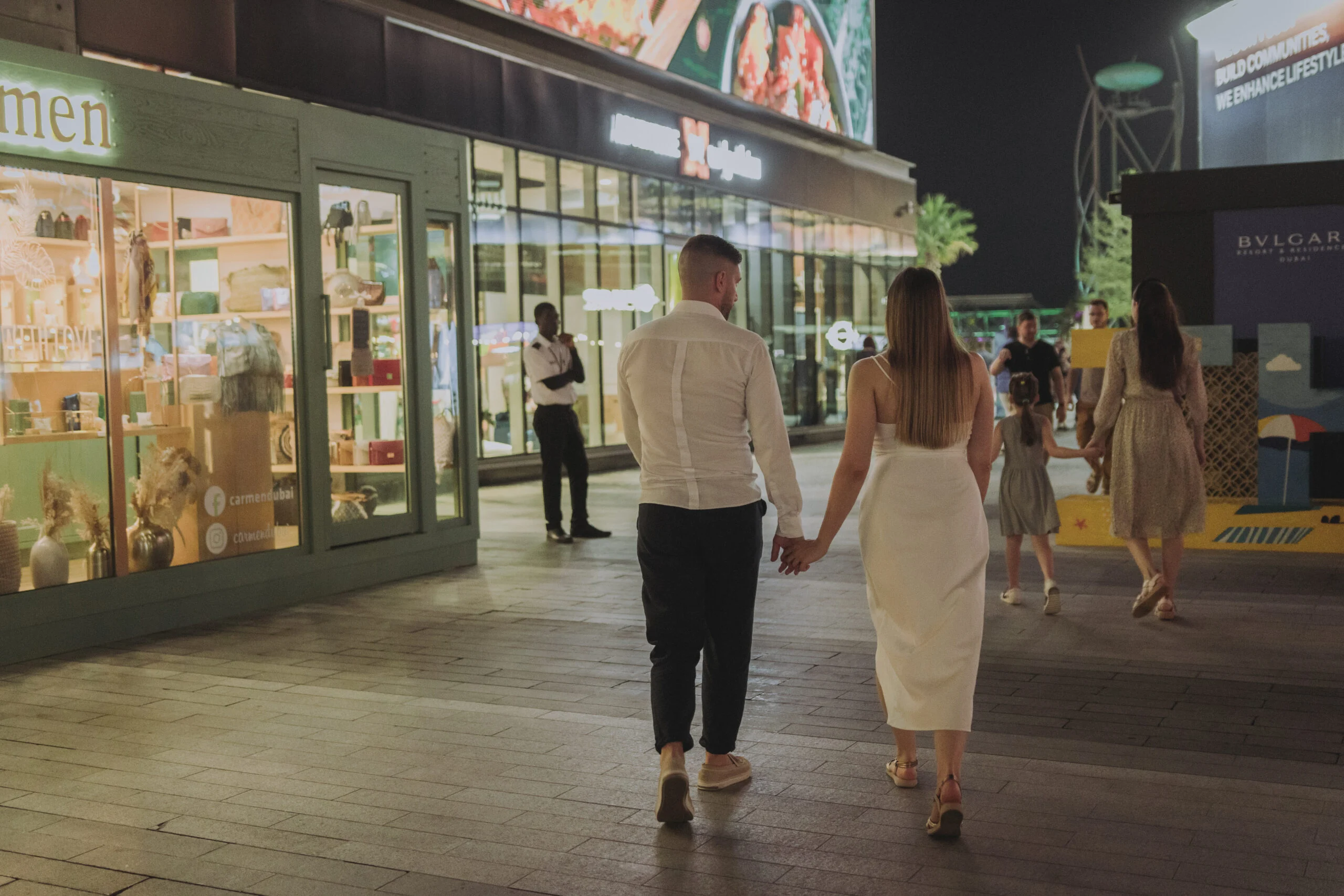 Couple walking hand in hand past lit shop fronts at night