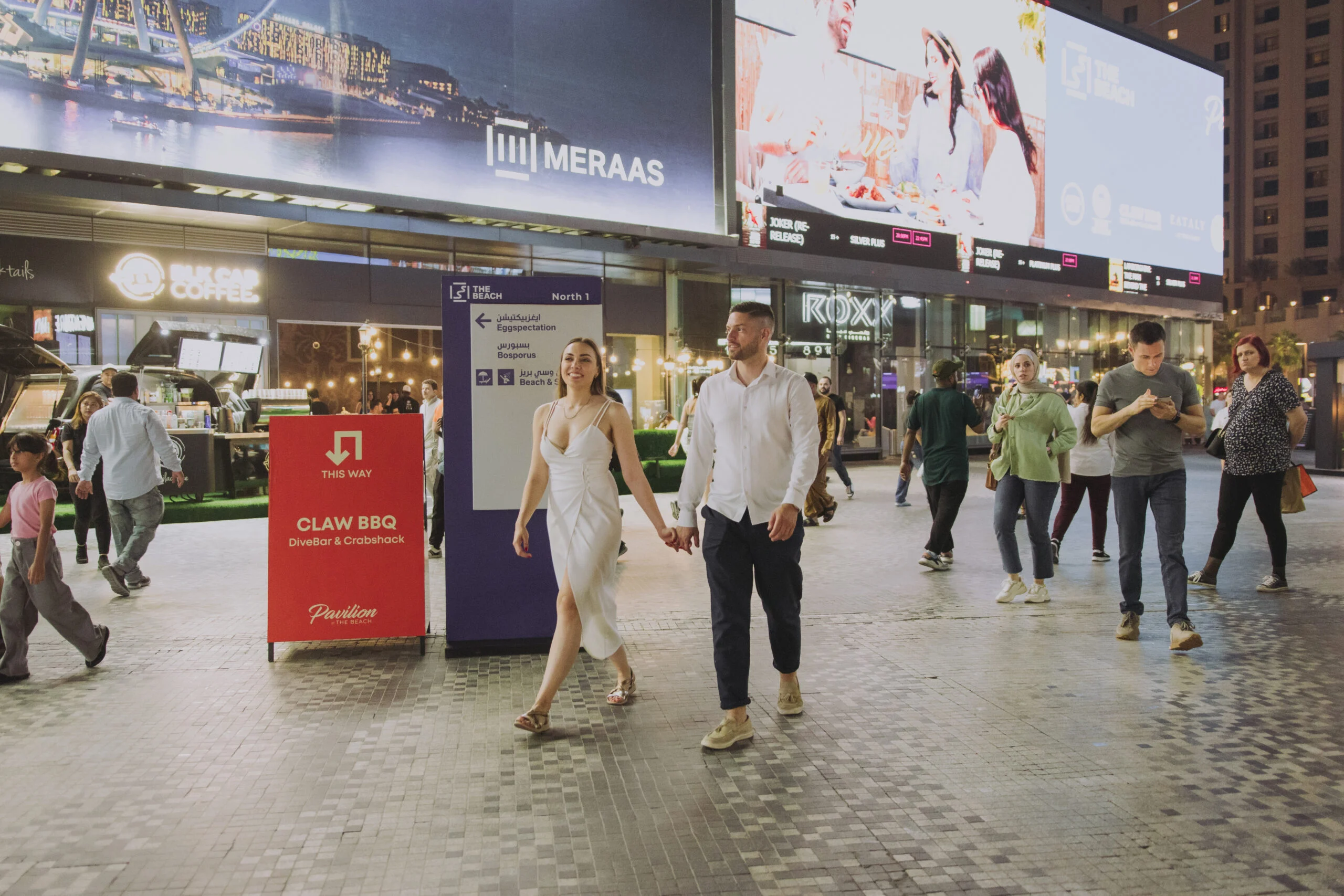 Couple walking through a crowd on the promenade at night
