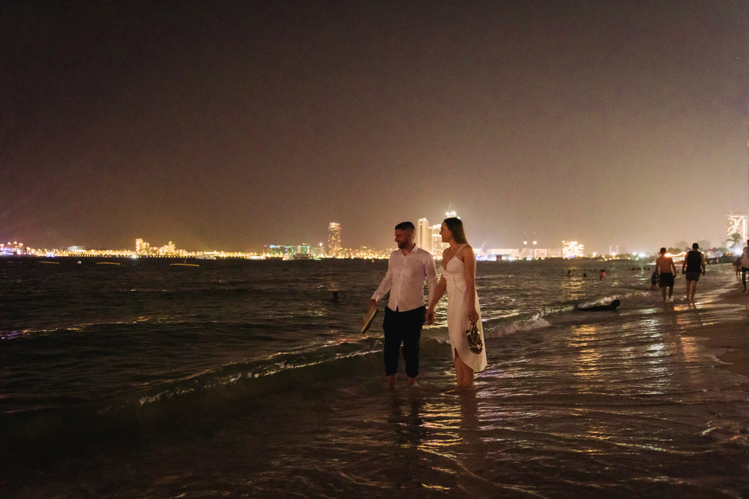 Couple standing in shallow water at night, the city lights beyond