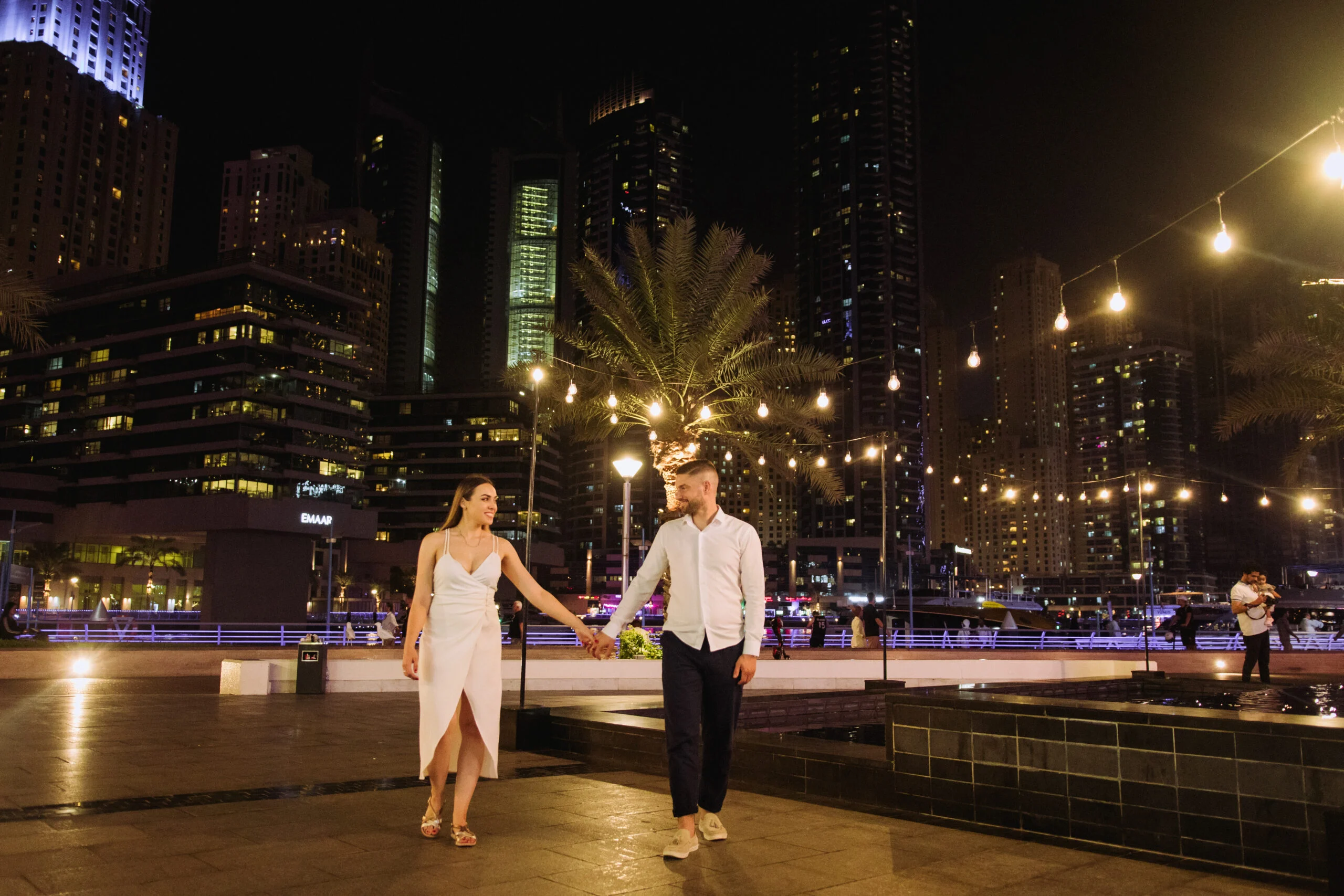 Couple by the water with the towers lit behind them