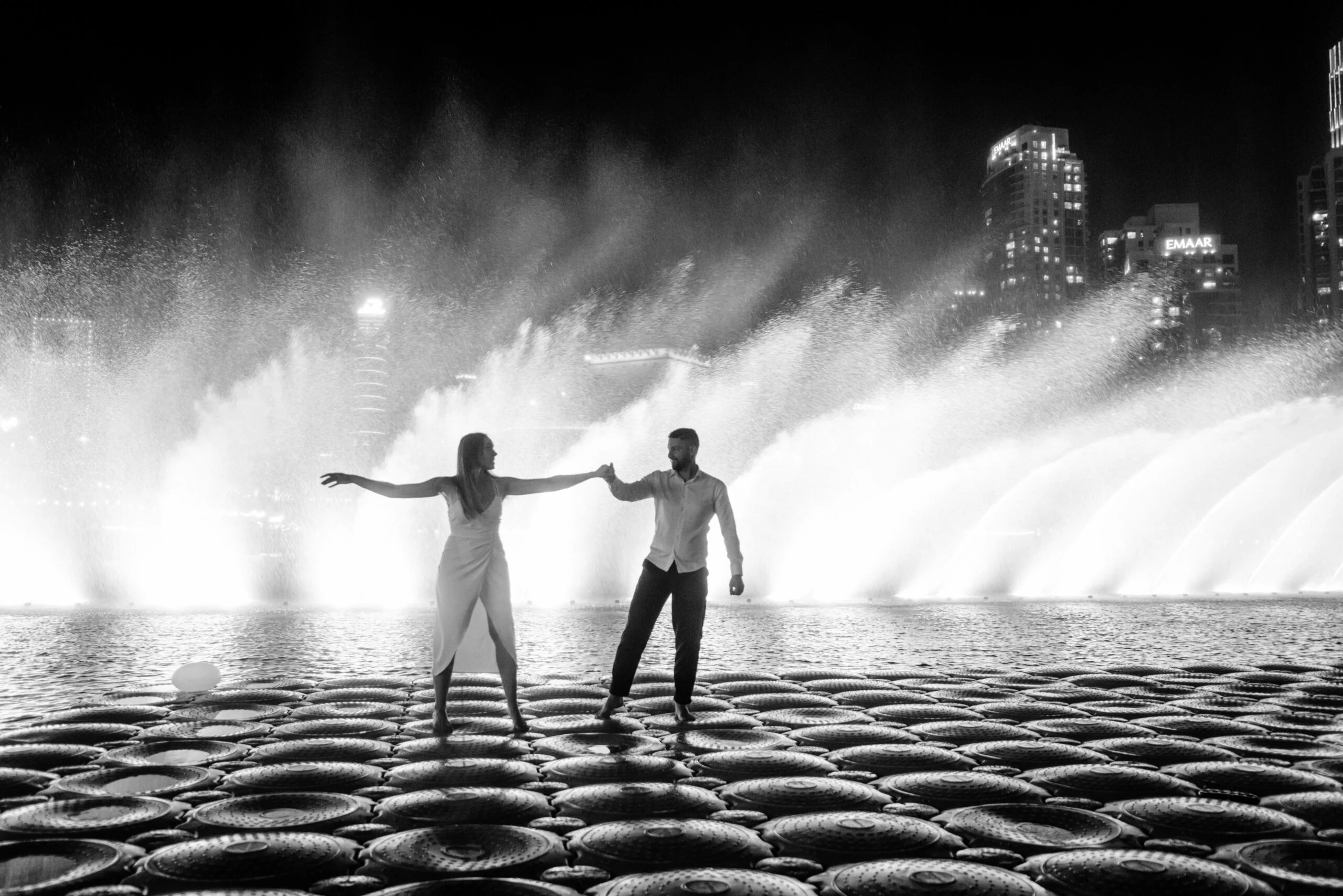 Black and white photograph of the couple with arms outstretched before the fountains