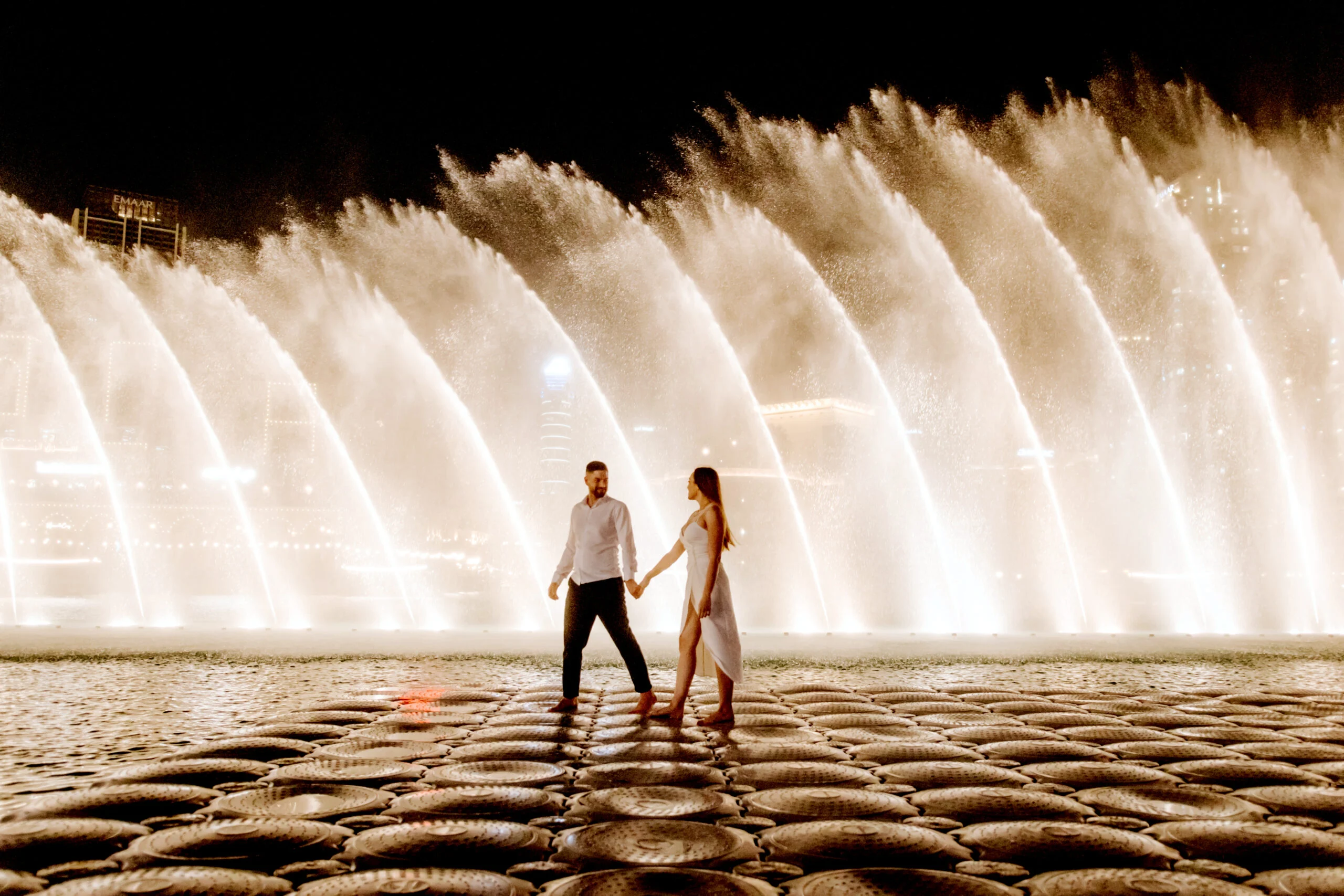 Couple standing apart in front of the lit fountains