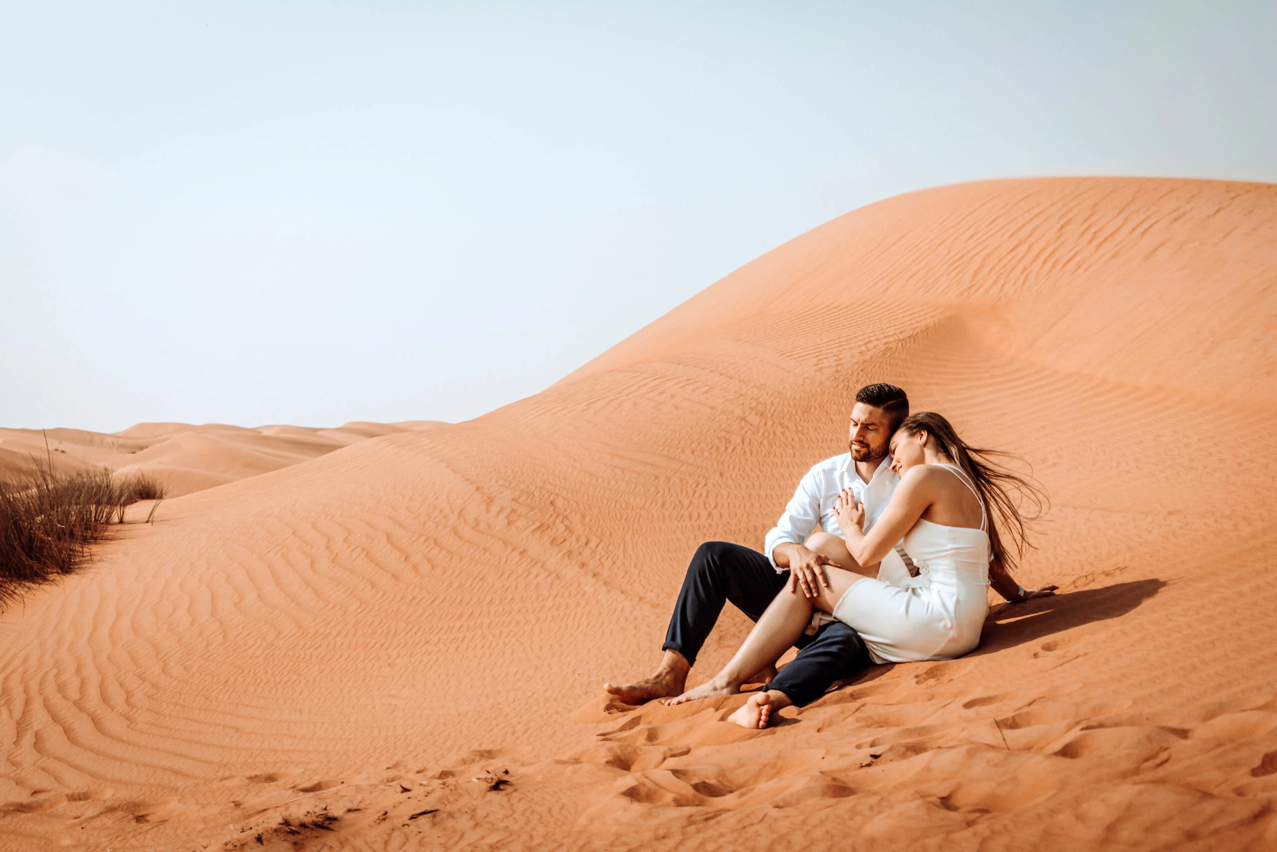 Couple sitting on the sand, the woman's hair in the wind