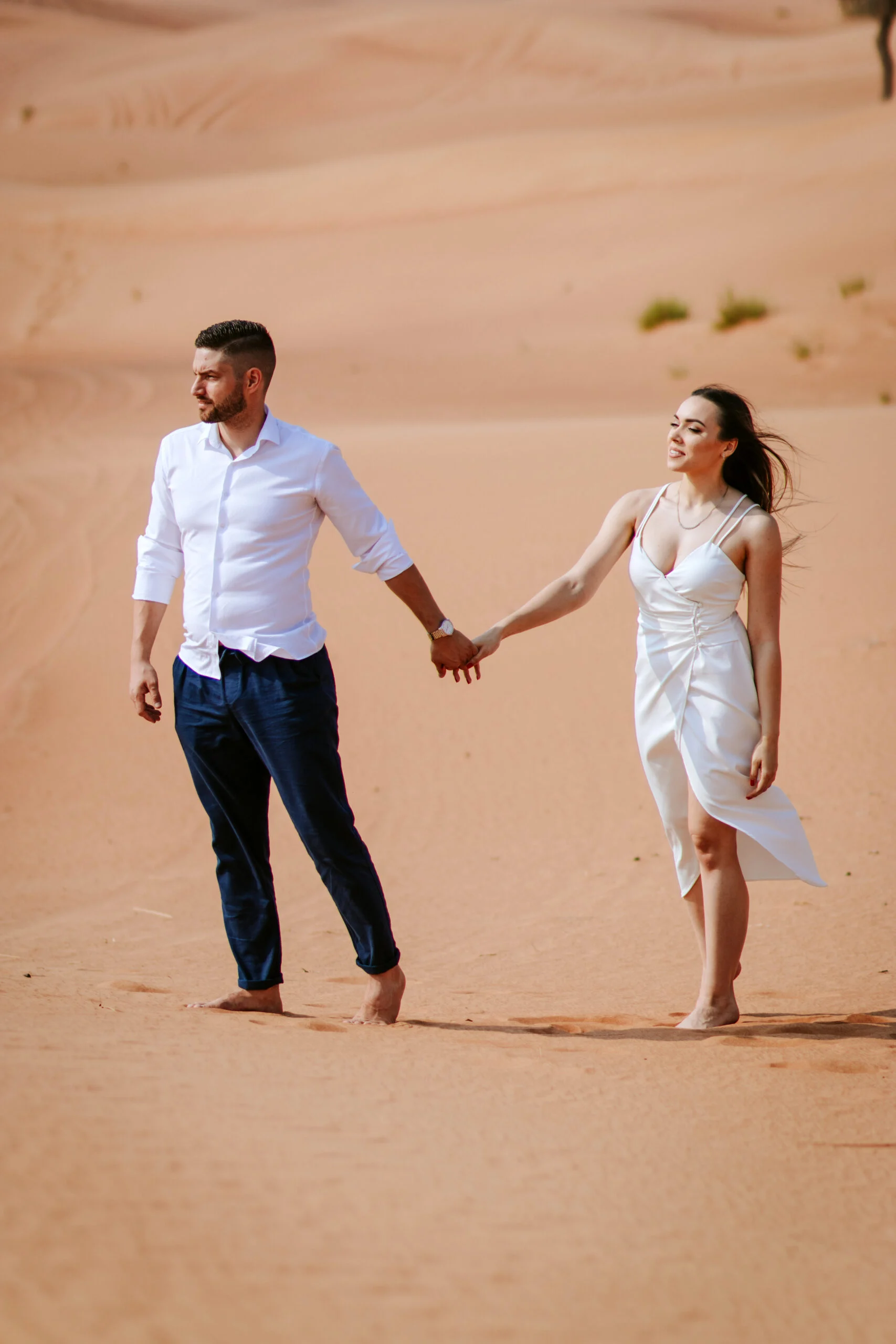 Couple walking hand in hand, the woman's dress lifted by the wind