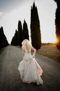 Bride turning on the cypress-lined road, the low sun behind her