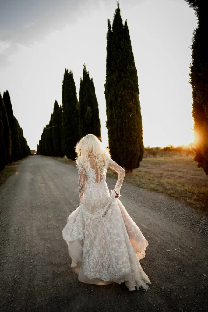Bride turning on the cypress-lined road, the low sun behind her