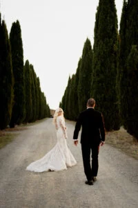 Bride and groom walking away along a road lined with cypresses
