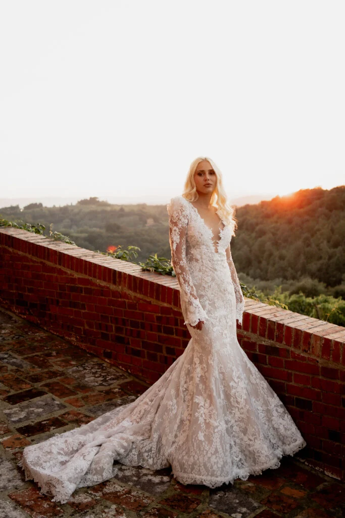 Bride standing on a brick terrace with the Tuscan hills behind her at sunset