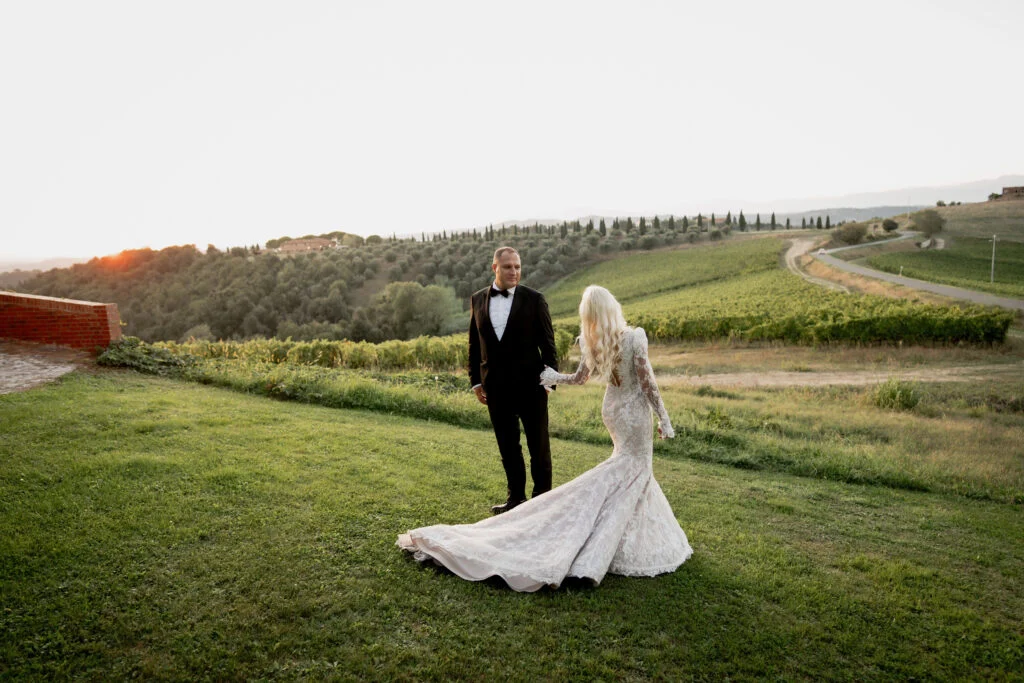 Bride and groom walking across a lawn above the vineyards at sunset