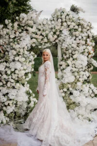 Bride standing in front of a tall arch of white flowers