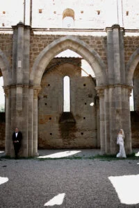 Bride and groom standing apart in the ruins, separated by stone arches