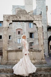 Bride standing on the square below the stone towers of a Tuscan hill town