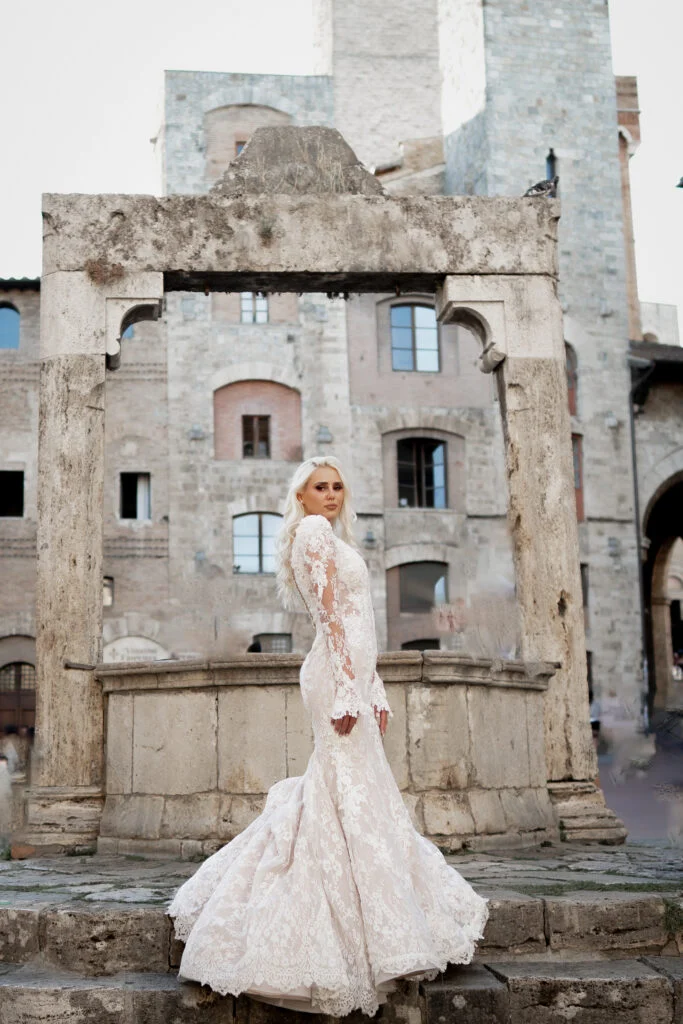 Bride standing on the square below the stone towers of a Tuscan hill town