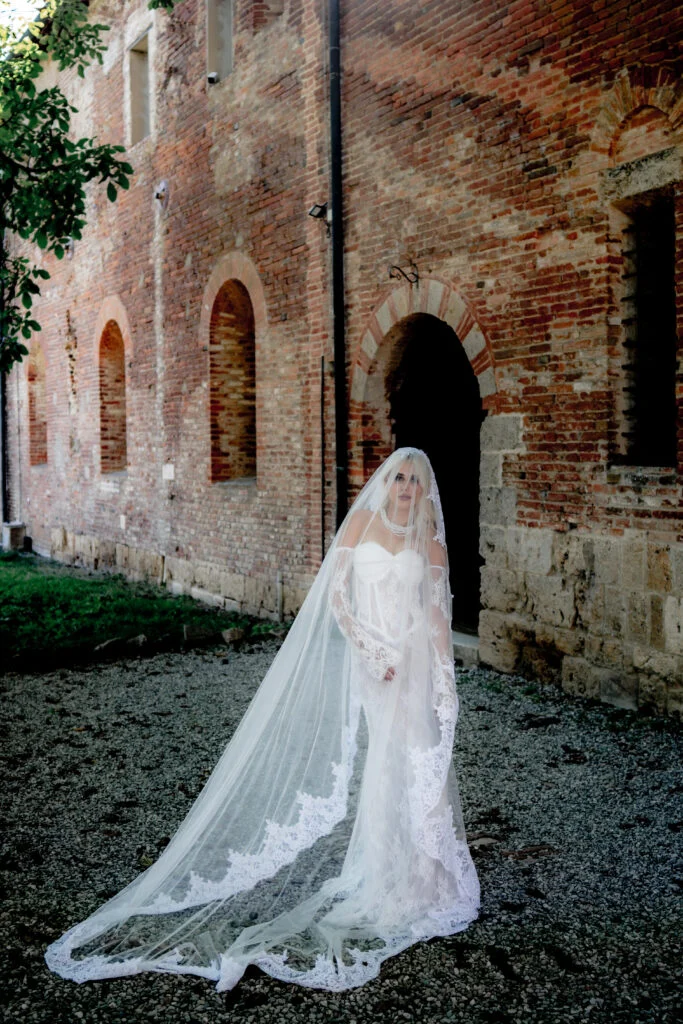 Bride with her lace veil spread out in front of a weathered brick wall