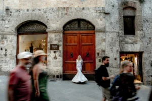 Bride passing an old wooden doorway as people walk by
