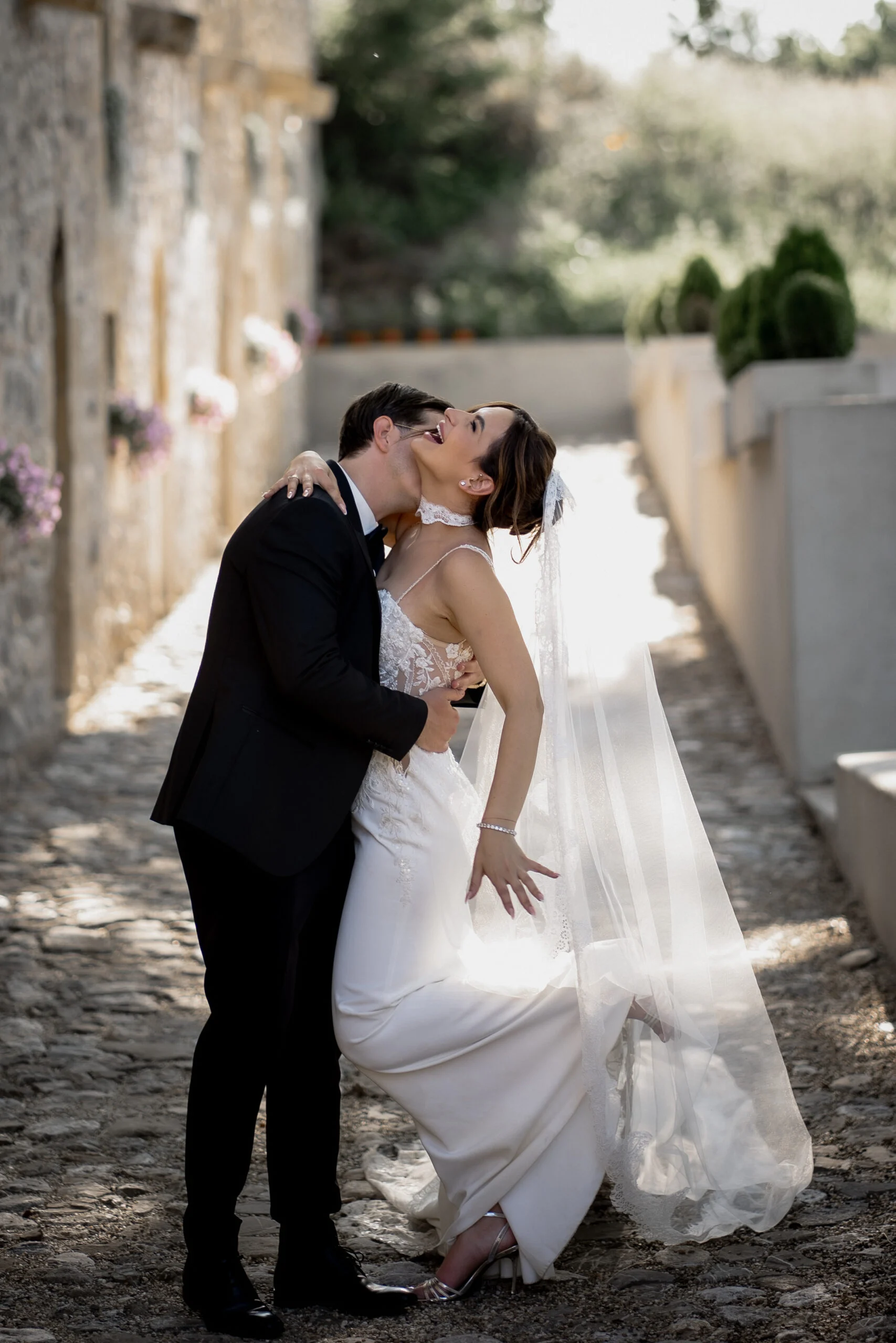 Bride and groom kissing in a narrow cobbled lane, her veil trailing behind her