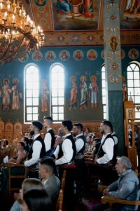 Guests in traditional Greek dress standing in a painted Orthodox church