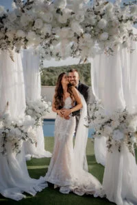 Bride and groom embracing under the floral arch, the pool behind them