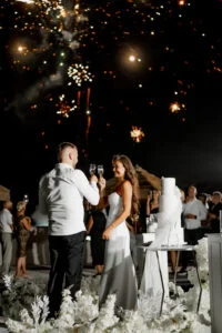 Bride and groom cutting the cake as fireworks go off behind them