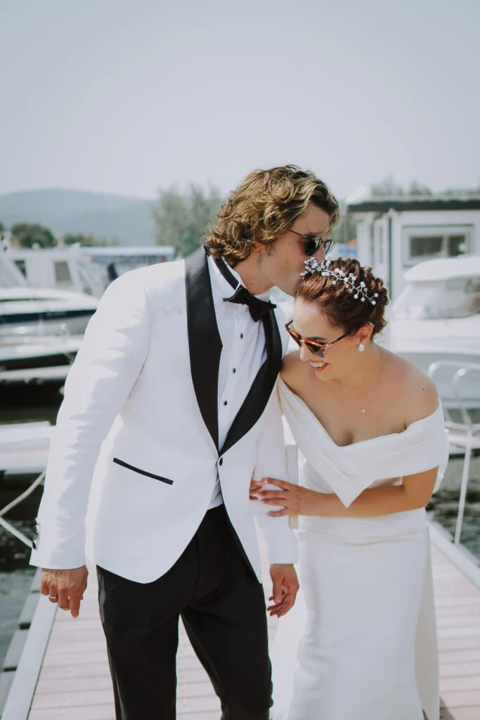 Groom leaning in to kiss the bride on the pontoon, boats behind them
