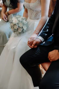Bride and groom holding hands during the ceremony, her bouquet in her lap