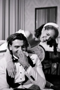 Black and white frame of the bride leaning over the groom's shoulder, both laughing