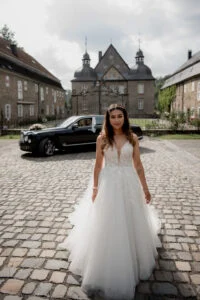 Bride standing in front of the manor house in Germany, beside a dark car