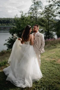 Bride and groom embracing on the grass beside a lake