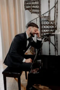 Groom at a grand piano beneath an ornate wrought-iron spiral staircase