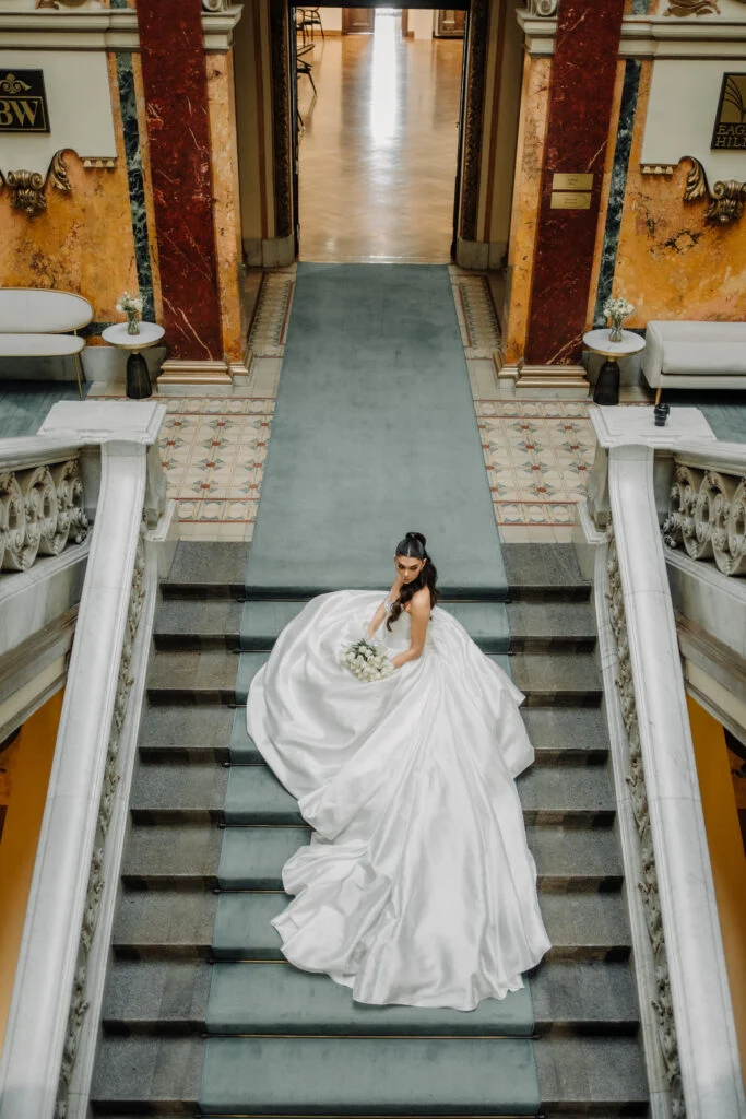Bride walking up a marble staircase with her long train behind her