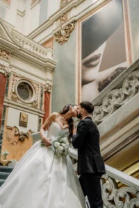 Bride and groom face to face on a gallery framed by painted panels and gilded stucco