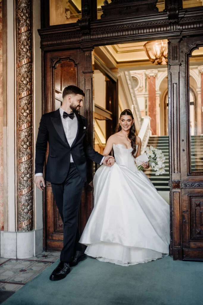 Bride and groom walking together through a dark wood-panelled entrance hall in Belgrade