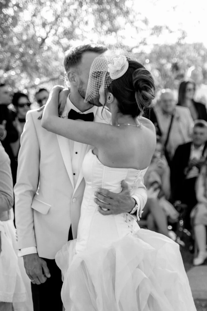 Black and white photograph of the couple embracing after the ceremony, guests around them