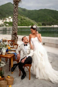 Bride sitting on the groom's lap at the table by the sea