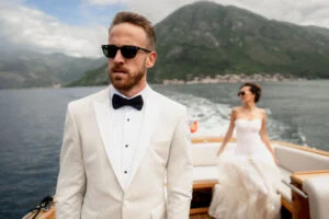 Groom looking at the camera as the bride sits at the stern of the boat