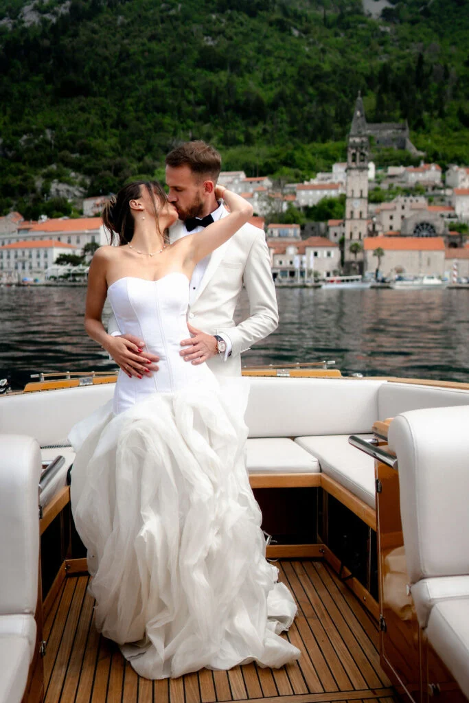 Bride and groom on the boat with the stone houses of Perast behind them