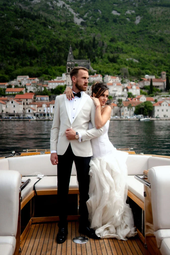 Bride and groom standing on the boat with the town of Perast behind them