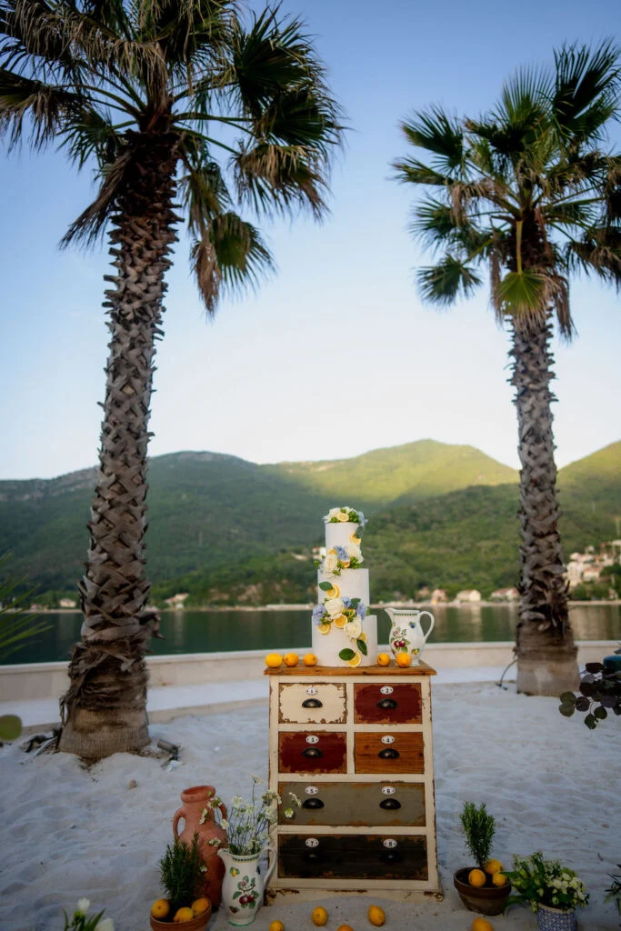 Wedding cake on a wooden dresser between two palms above the bay