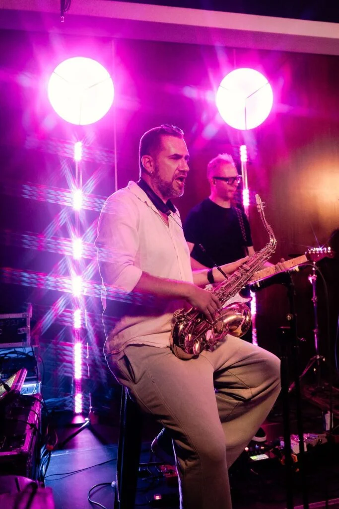 Saxophonist performing on the stage under pink and violet lights