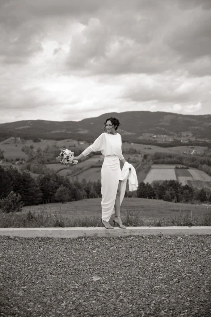 Black and white photograph of the bride walking a mountain road, hills behind her