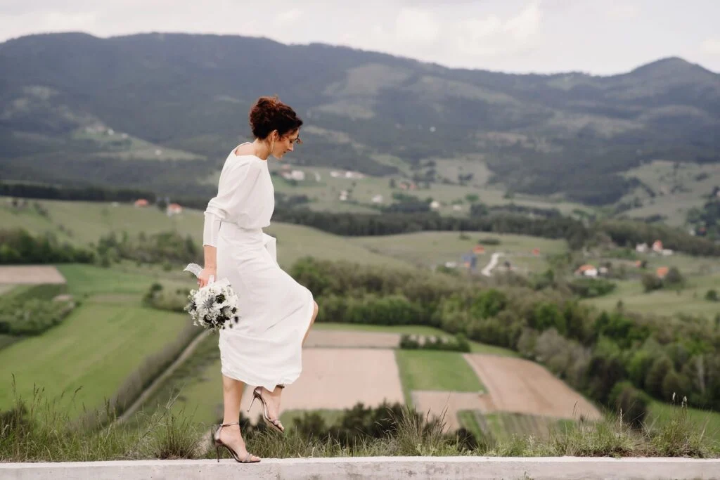Bride at a low wall with the green hills of western Serbia behind her